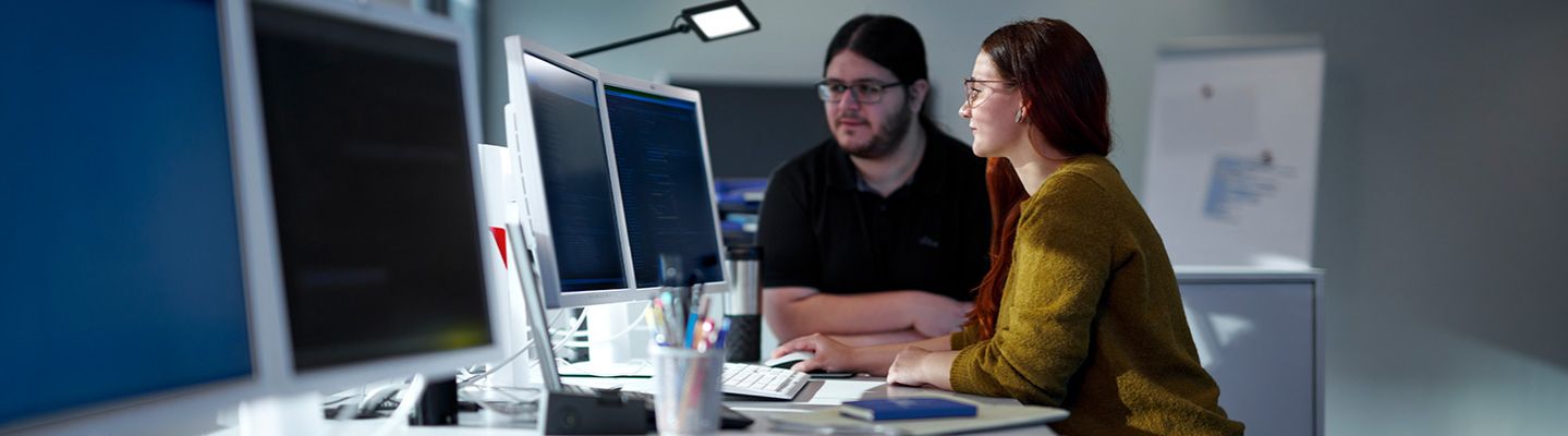Eine Technikerin und ein Techniker sitzen an einem Schreibtisch vor einem Computer